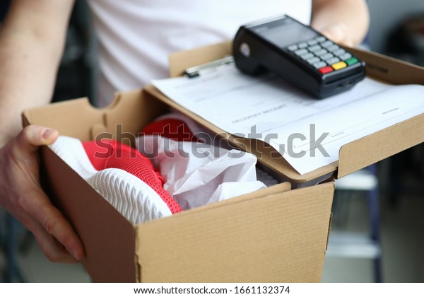 Man\
holds box with sneakers terminal for payment. Buyer can pay from\
home or in car. Postal company uses portable terminal to pay by\
credit card. Settlement with courier online\
store