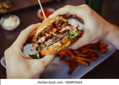 Mannen holder burger med hender og søtpotet pommes frites og dips på bakgrunn i kafeen