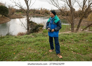 Man holds camera while standing by a lake surrounded by trees