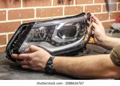 A Man Holds A Car Headlight After Repair. Car Repair And Tuning. Headlight Repair. Restoration Of Automotive Optics.
