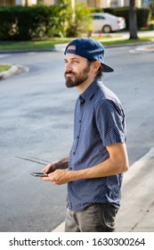 A Man Holds A Cell Phone In His Hands And Looks At The Street, Waiting For His Ride Share Vehicle.