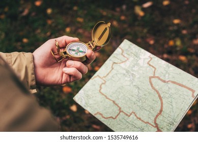 A man holds a compass and a paper map in his hand and is guided by the area, autumn forest, walk,hiking - Powered by Shutterstock