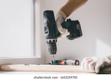 A man holds a cordless screwdriver in his hand and wraps the screw in a Board. Carpenter working with an electric screwdriver on the work bench
