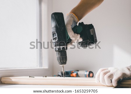 A man holds a cordless screwdriver in his hand and wraps the screw in a Board. Carpenter working with an electric screwdriver on the work bench