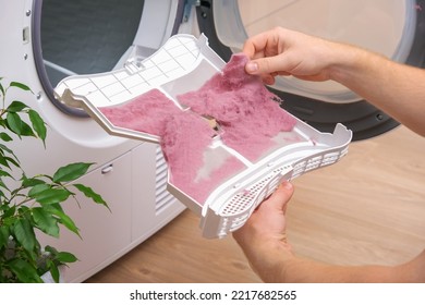 A man holds a dirty dryer filter. A man collects lint, hair, wool from the filter of a drying machine. Red lint on the dryer filter. Dirty filter dryer.