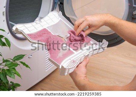 A man holds a dirty dryer filter. A man collects lint, hair, wool from the filter of a drying machine. Red lint on the dryer filter. Dirty filter dryer. tumble dryer