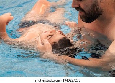 A Man Holds A Disabled Child During Aquatic Therapy In A Swimming Pool.