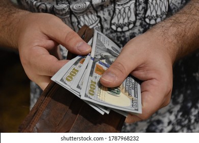 The man holds the dollars us, gets out the money of his wallet. Subsistence level, family budget, shop payment - Shutterstock ID 1787968232