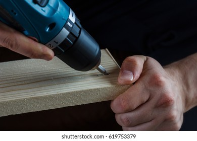 Man holds a drill in his hands and makes a hole in a wooden board