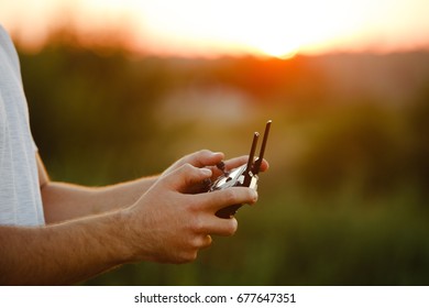 Man holds a drone remote controller in his hands. Close-up of quadrocopter RC during flight. Pilot takes aerial photos and videos with quad on sunset