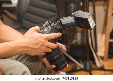 Man holds a DSLR camera with speedlight or flash attached.