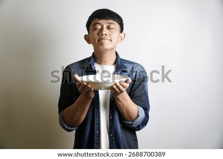 A man holds an empty plate while closing his eyes, as if smelling the delicious aroma of food.
