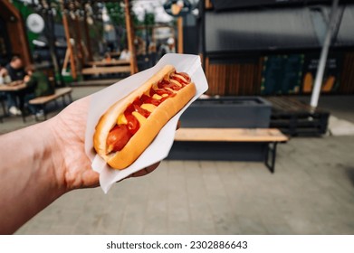 man holds fresh hot dog with sauce in hands. Street food, fast food outdoor - Powered by Shutterstock