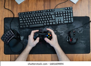 A Man Holds A Game Pad Around A Gaming Keyboard In His Hands, A Game Pad Mouse. Top View
