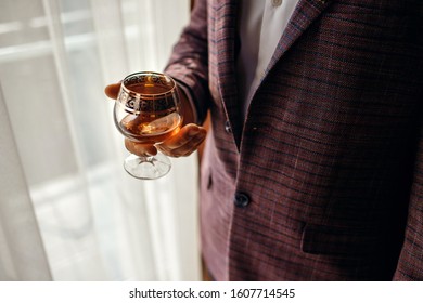 A man holds a glass with whiskey, dressed in a classic jacket, a beautiful glass with cognac, a respectable man