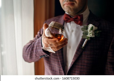 A man holds a glass with whiskey, dressed in a classic suit, a beautiful glass with cognac, a respectable man, male style, alcohol