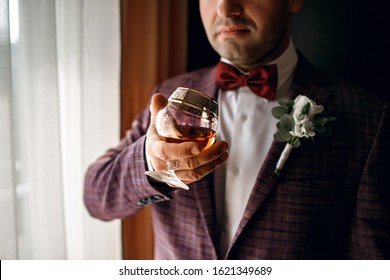 A man holds a glass with whiskey, dressed in a classic suit, a beautiful glass with cognac, a respectable man, male style, alcohol, a man stands near the window