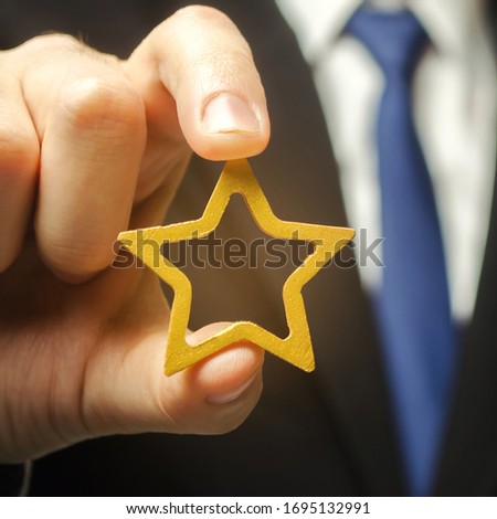 Man holds a golden star in his hand. Symbol of success and excellence. Good reputation, prestige, high recognition. Status, rating. Good ratings and reviews. VIP. Job promotion and career growth.