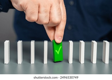 A man holds a green domino with a check mark. Checkpoint reached, milestone. Successfully completed. Ready for launch. Checking and verification. Start a business. A life stage that has been passed.