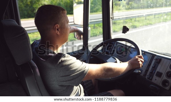 Man holds\
hand on the steering wheel and driving truck through countryside on\
a warm summer day. Profile of truck driver. Trucker inside at car.\
Side view Close up Slow\
motion.
