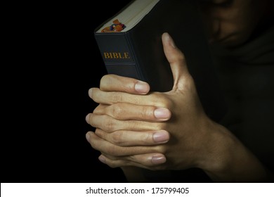 Man holds his bible with interlocked fingers to pray