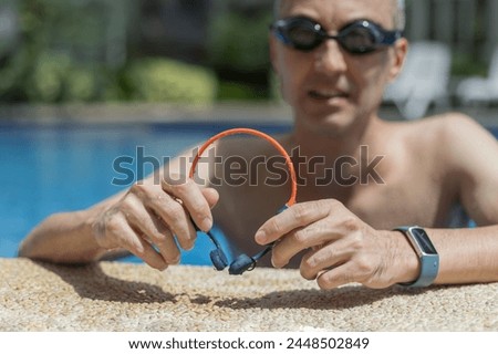A man holds his bone conduction headphones in hand, basking by the poolside, enjoying the sun-soaked ambiance while embracing the versatility of his audio gear.