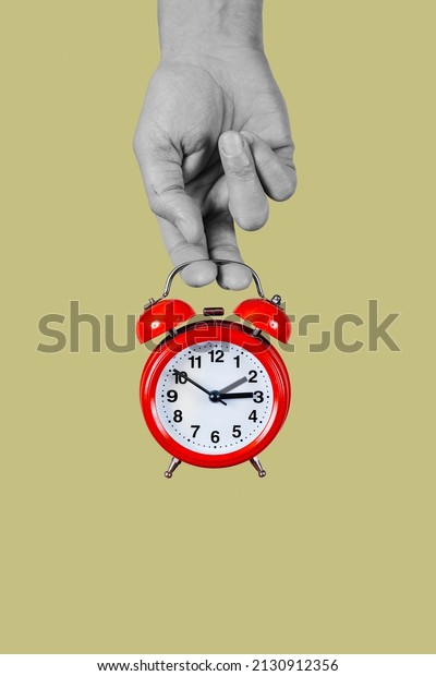 a man holds in\
his hand, in black and white, a classic red alarm clock, that is\
setting one hour backwards or forwards, at the beginning or the end\
of the summer time