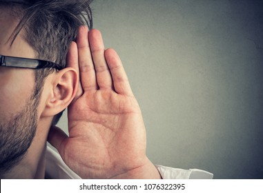 Mann hält seine Hand nahe Ohr und hört aufmerksam einzeln auf grauem Hintergrund