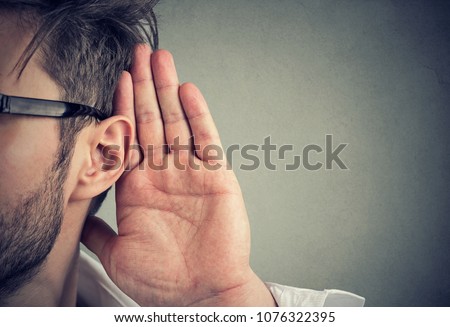 man holds his hand near ear and listens carefully isolated on gray wall background