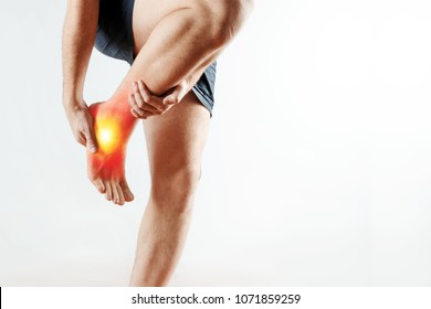 The man holds his hands to the ankle, the pain in his leg, the pain in the foot is highlighted in red. Light background. The concept of medicine, massage, physiotherapy, health. - Shutterstock ID 1071859259