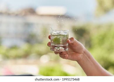Man holds in his hands a glass of homemade cocktail of hard seltzer with herbs in front of mountains. Summer wallpaper close up.