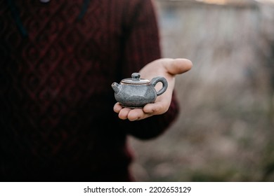 A man holds in his palm a small teapot  for a tea ceremony