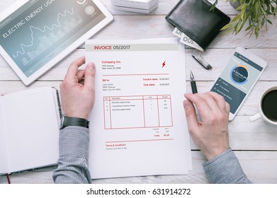 Man holds invoice of electric power usage over desk with tablet and smartphone with applications made in graphic program. - Powered by Shutterstock