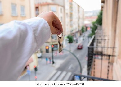 A Man Holds Keys In A House With Buildings In The Background. Real State Concept