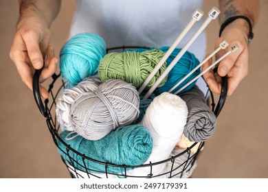 A man holds a large basket with colorful yarn. Knitting needles and hooks for knitting. - Powered by Shutterstock