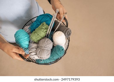 A man holds a large basket with colorful yarn. Knitting needles and hooks for knitting. - Powered by Shutterstock