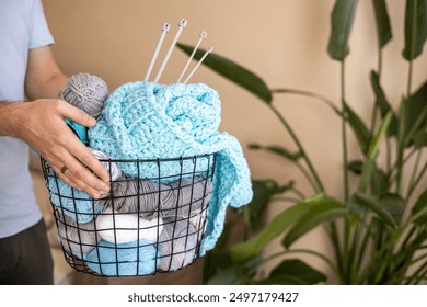 A man holds a large basket with colorful yarn. Knitting needles and hooks for knitting. - Powered by Shutterstock