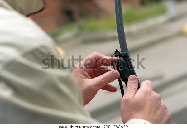 Man holds the latch on the wiper blade\
holder with his fingers on a blurry\
background