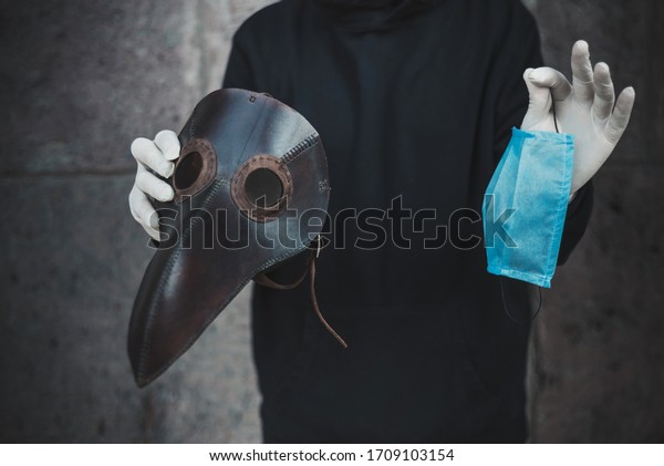 Man holds a mask of plague doctor and disposable\
medical mask.