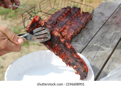 A Man Holds Meat On Ribs With Cooking Tongs At A Picnic