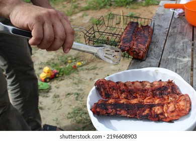 A Man Holds Meat On Ribs With Cooking Tongs At A Picnic