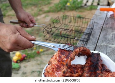 A Man Holds Meat On Ribs With Cooking Tongs At A Picnic