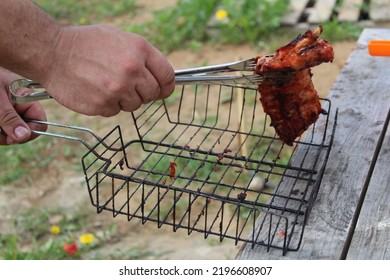 A Man Holds Meat On Ribs With Cooking Tongs At A Picnic