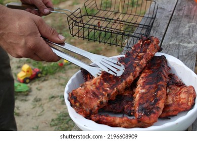 A Man Holds Meat On Ribs With Cooking Tongs At A Picnic