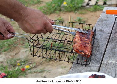 A Man Holds Meat On Ribs With Cooking Tongs At A Picnic