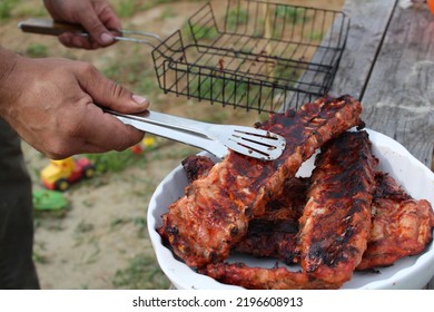 A Man Holds Meat On Ribs With Cooking Tongs At A Picnic