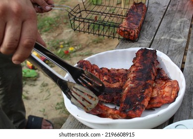 A Man Holds Meat On Ribs With Cooking Tongs At A Picnic