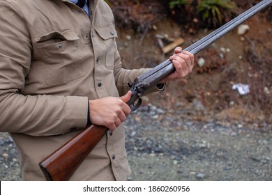 A man holds an old, antique, double-barrel shotgun to his waist, pointing the barrel downrange, ready to load. Outdoor range in Squamish, British-Columbia