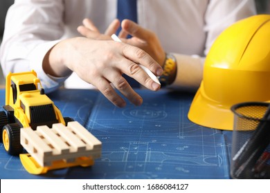 Man holds pencil, on table yellow helmet and truck. Construction calculation for use rented equipment. Procurement building material for work. Transportation wooden blocks automobile