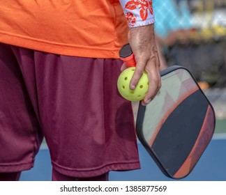 Man Holds Pickleball Paddle And Ball In One Hand.